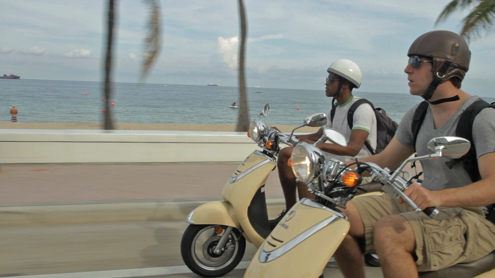 Side view of two men on scooters on a beach