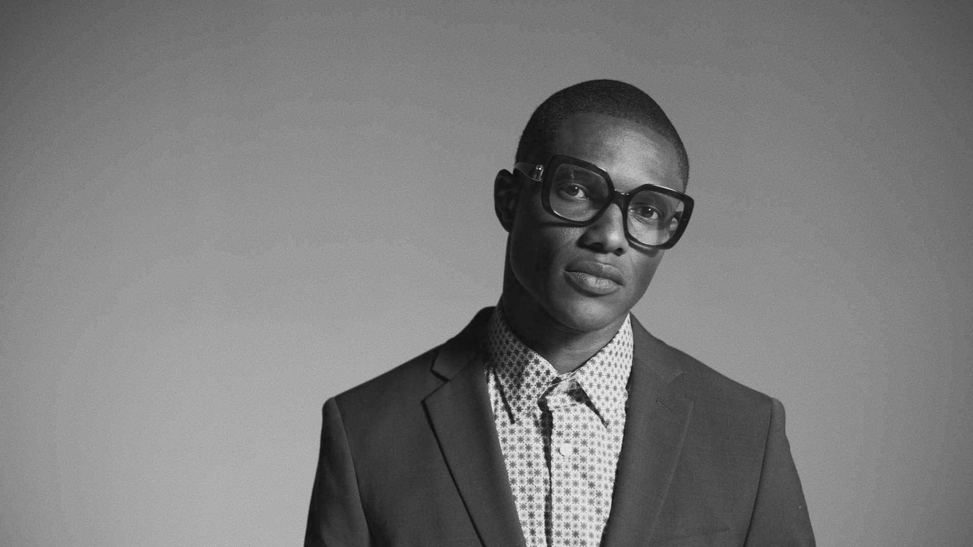 Black and white image of model wearing a suit and glasses