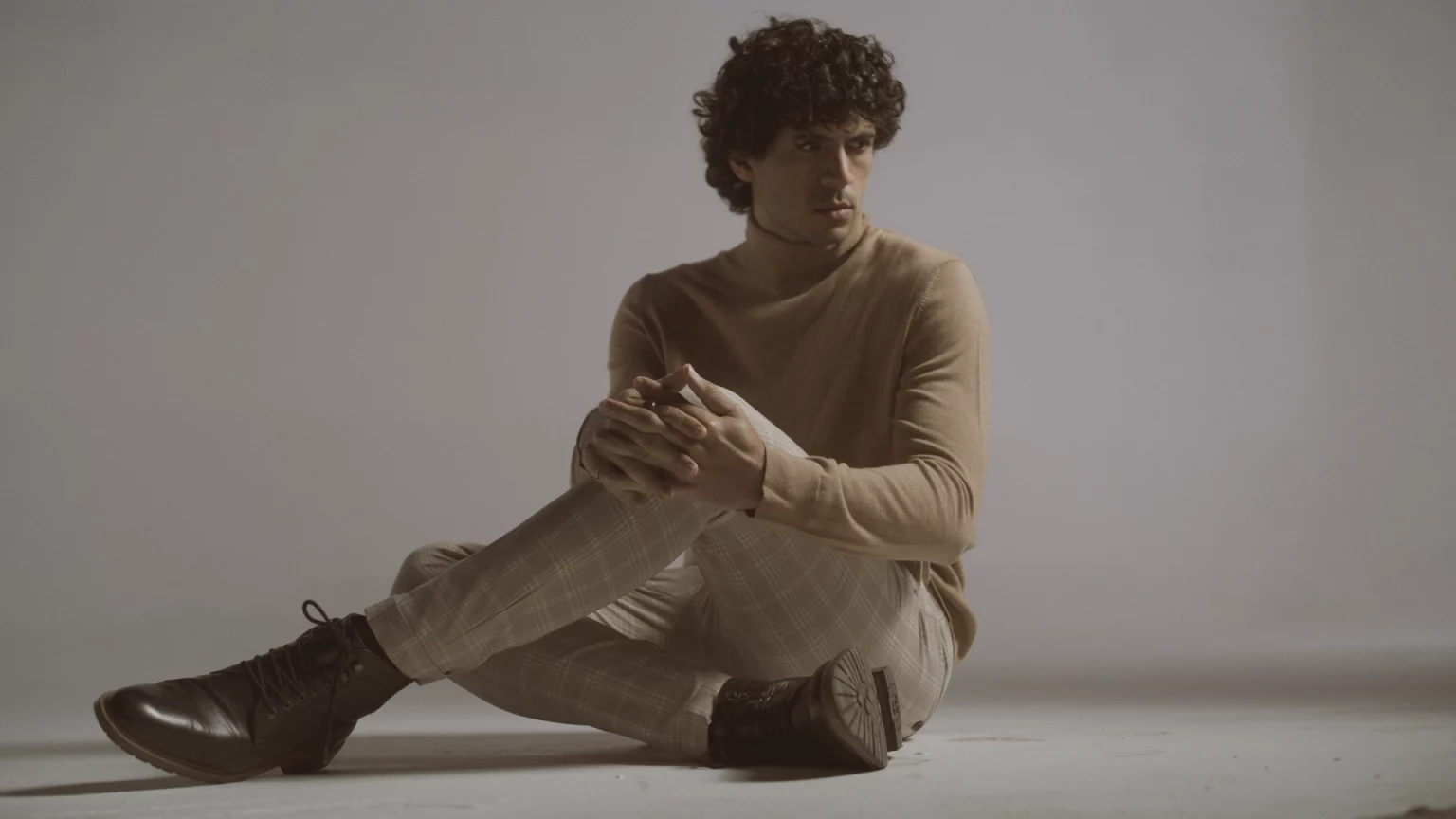 Man With Curly Hair Wearing Beige Sweater And Patterned Pants