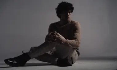 Man with curly hair wearing beige sweater and patterned pants