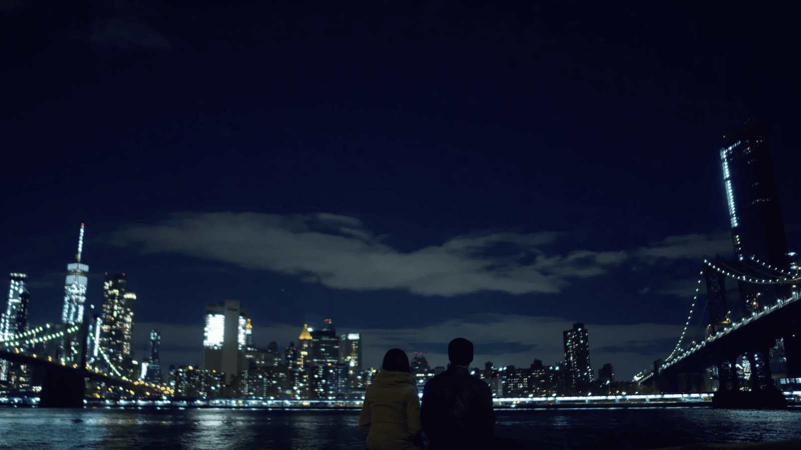 View from behind of man and woman looking out over the city at night