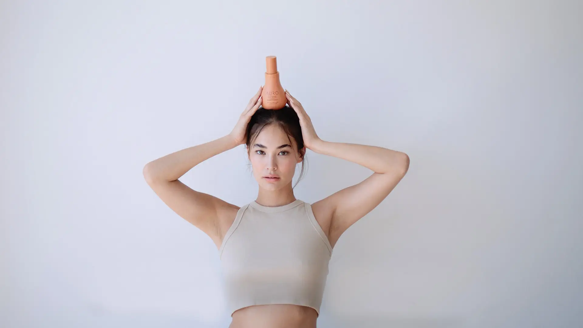 Female model holding Auro Skincare bottle on head