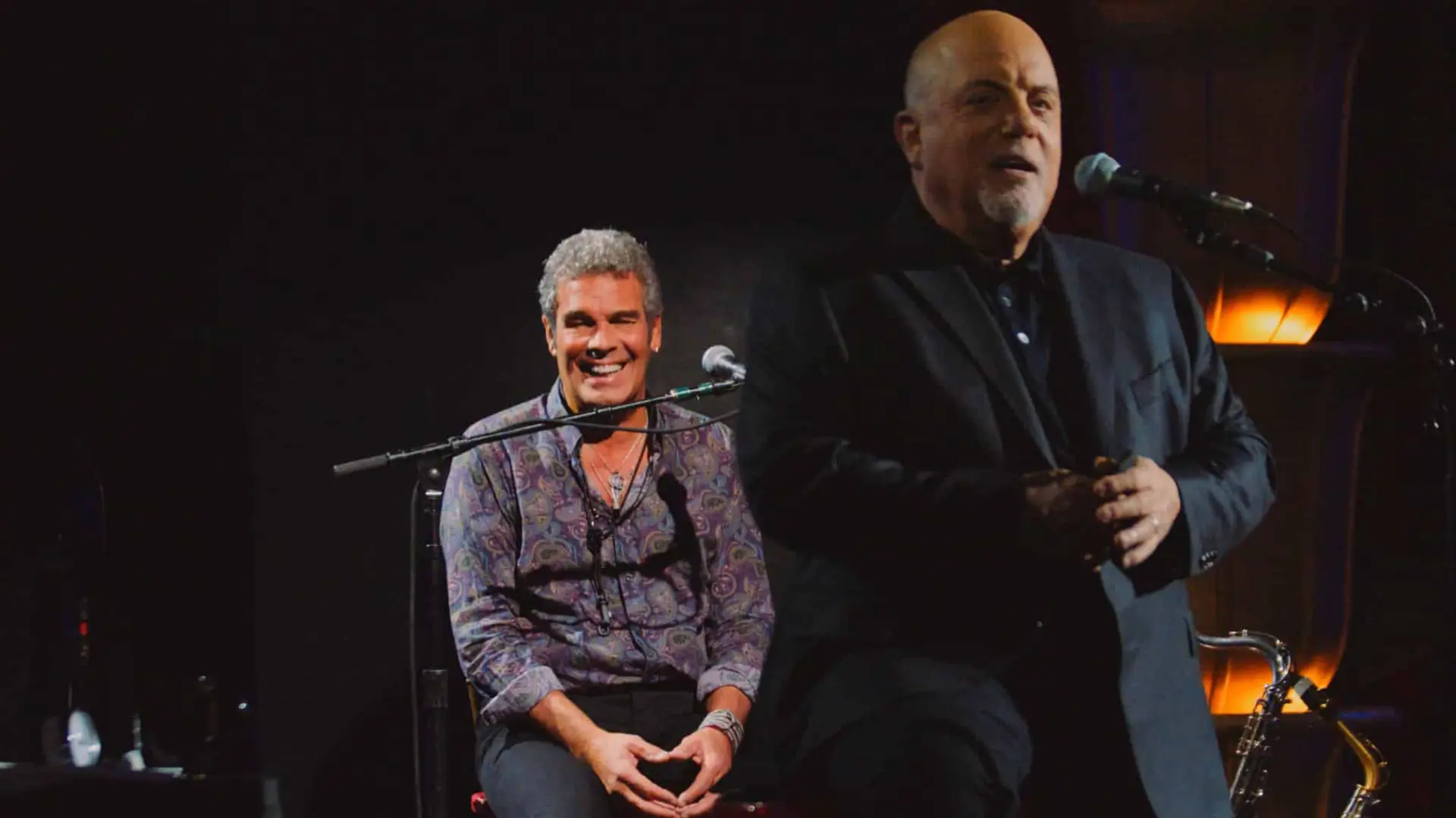Billy Joel 2 Billy Joel talks to audience with man behind him smiling