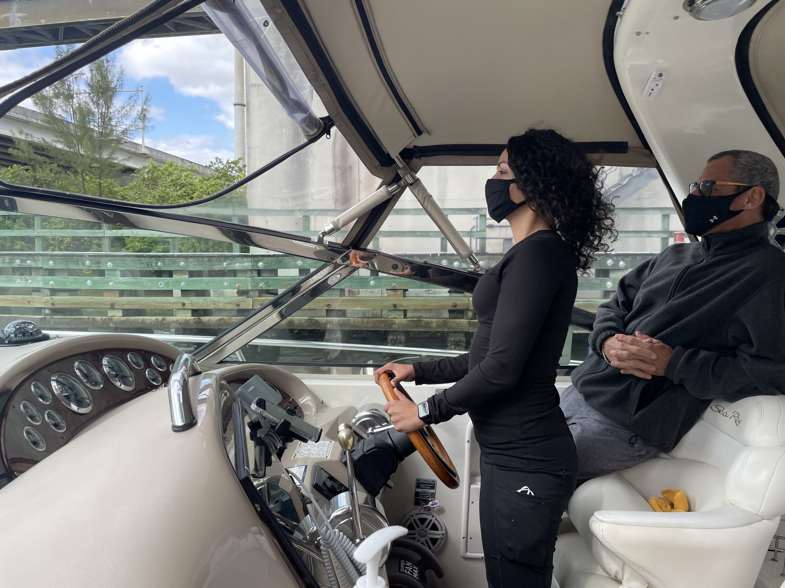 Side profile of woman wearing black outfir driving a yacht with man sitting next to her looking on