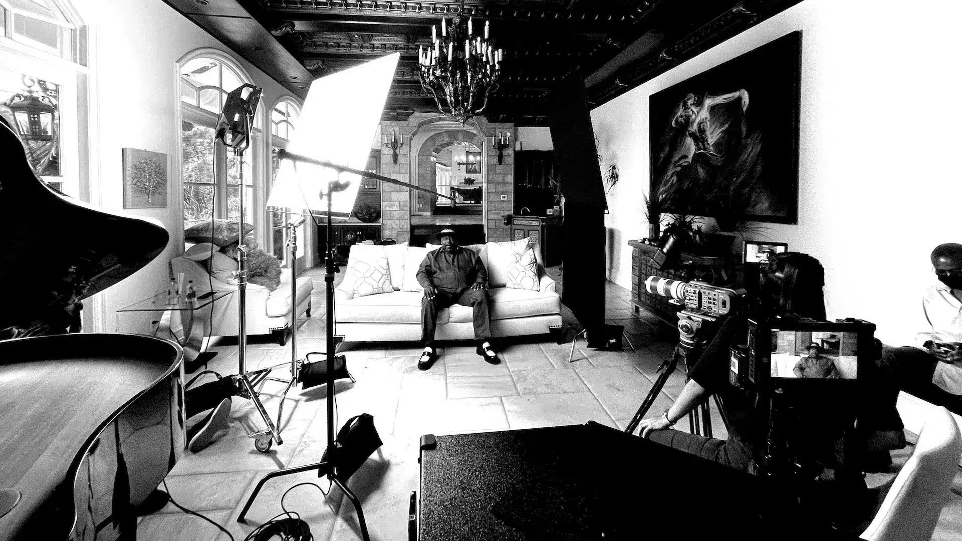 Cedric The Entertainer sitting on a set surrounded by crew and equipment black and white