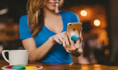 Woman wearing light blue shirt using a cell phone with white coffee cup and macaroons nearby