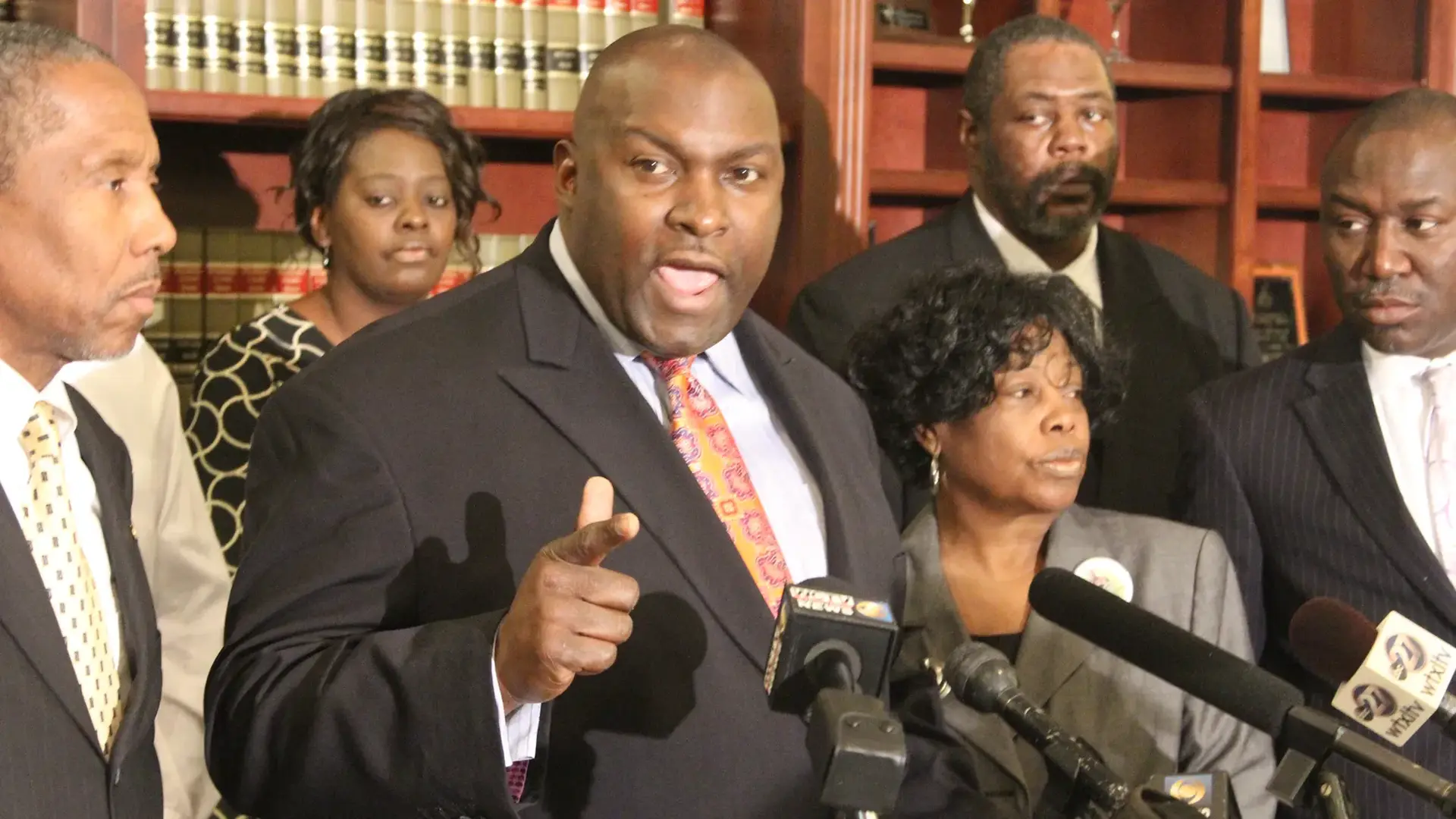 Daryl Parks 3 Daryl Parks speaking into a mic behind a podium surrounded by other people