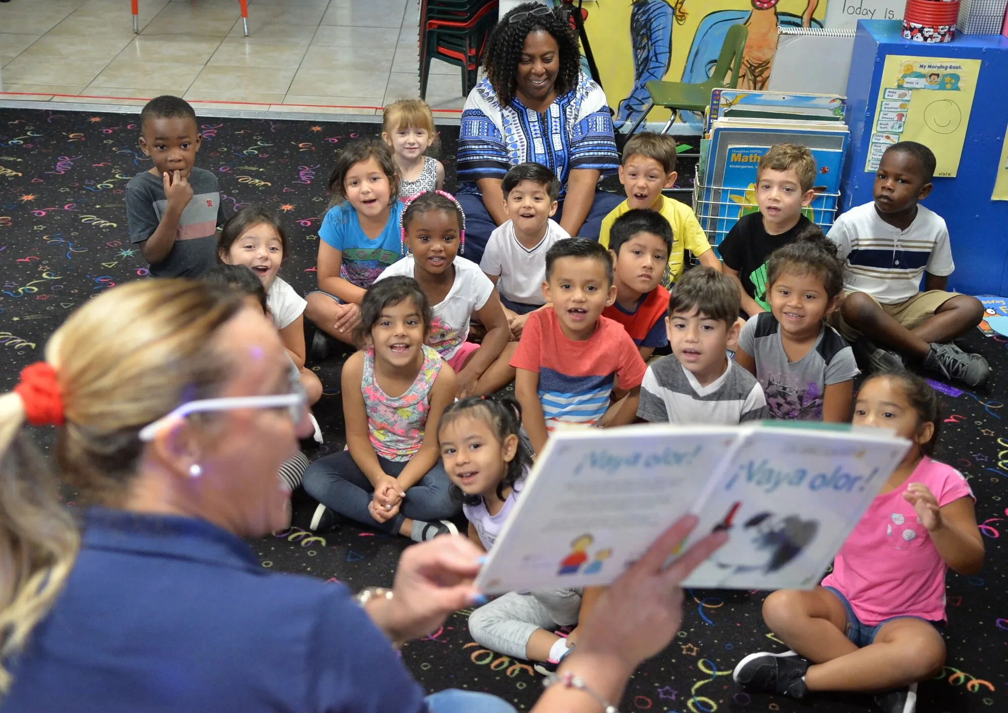 Florida Department of Children and Families 3 Florida Children System of Care preschool teacher reading bilingual book to diverse classroom of children