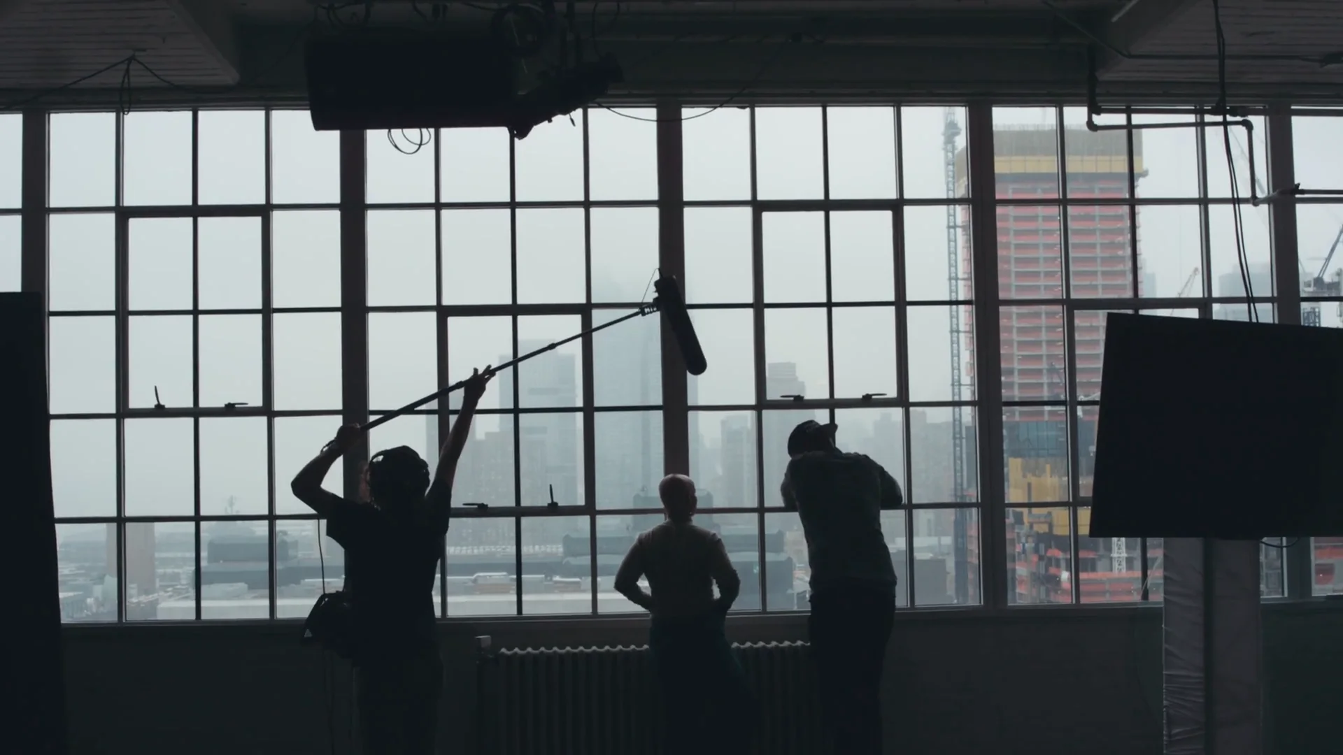 Location line of a commercial video budget, crew with a boom mic at a tall window over the skyline