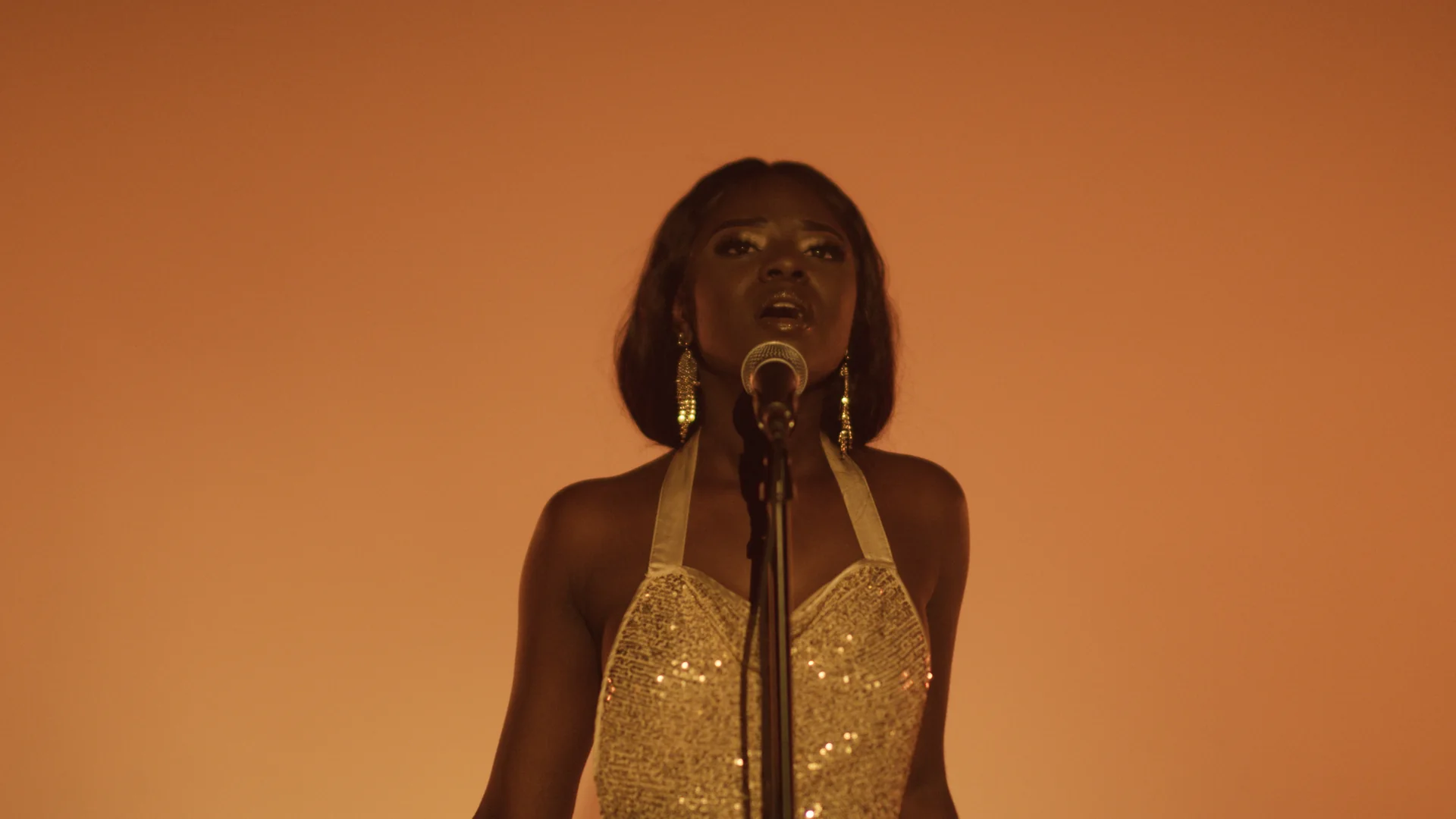 What a Music Video Production Budget Covers 2 Singer performing at a vintage mic against a warm orange backdrop in a music video by C&I Studios